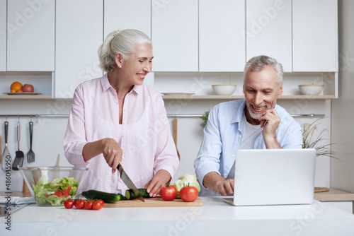Man use laptop while wife cut cucumber for salad