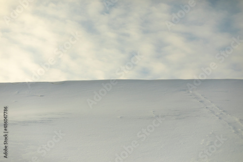 Snowy slope against sky. Avalanche of snow on mountain ridge. Winter weather.