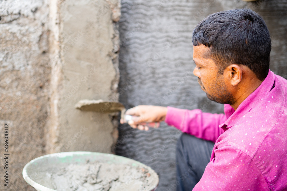 Indian daily wager busy on wall plaster work at construction side with safety gloves - concept of hard working, concentrated and constucation labour. Indian daily wager busy on wall plaster work at construction side with safety gloves - concept of hard working, concentrated and constucation labour.