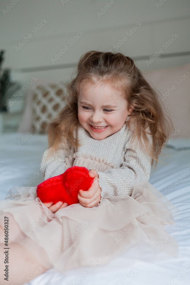 Adorable little girl of 3 years old with blue eyes holds a red plush heart in her hands. Valentine's Day. Emotional child. Adorable little girl of 3 years old with blue eyes holds a red plush heart in her hands. Valentine's Day. Emotional child.
