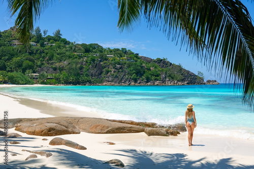 A tropical travel concept banner with copy space showing a woman in swimsuit walking down a paradise beach with palm trees and turquoise sea