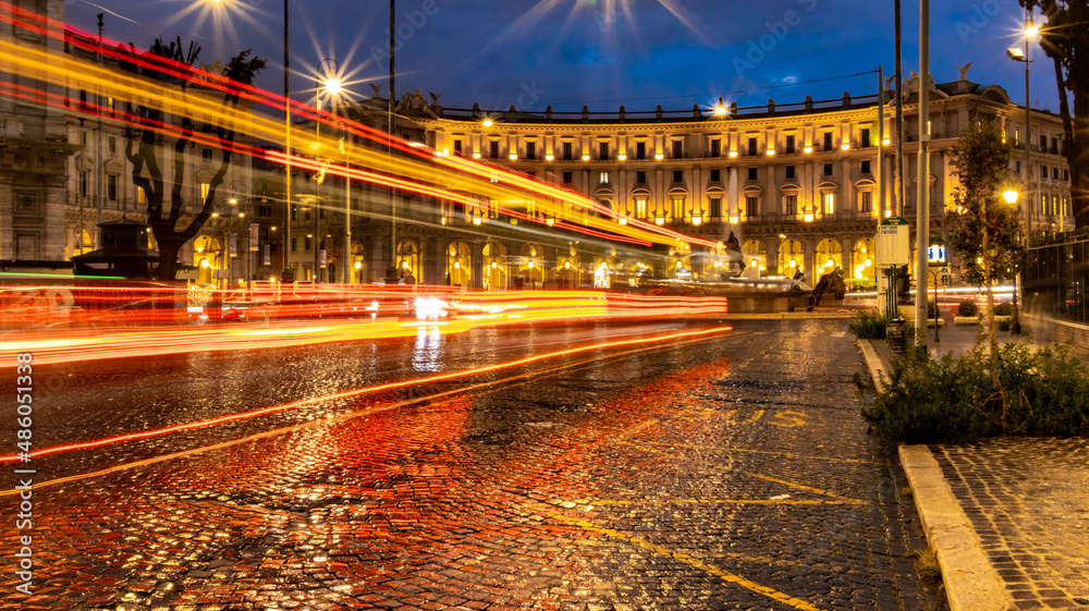 Cars light trails in the evening square in Rome right after the rain. Night traffic routes. Motion blur. Cityscape.