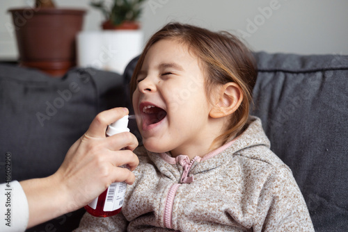 Close up of girl portrait and mother hand with spray for throat. Kids flu medical treatment concept 