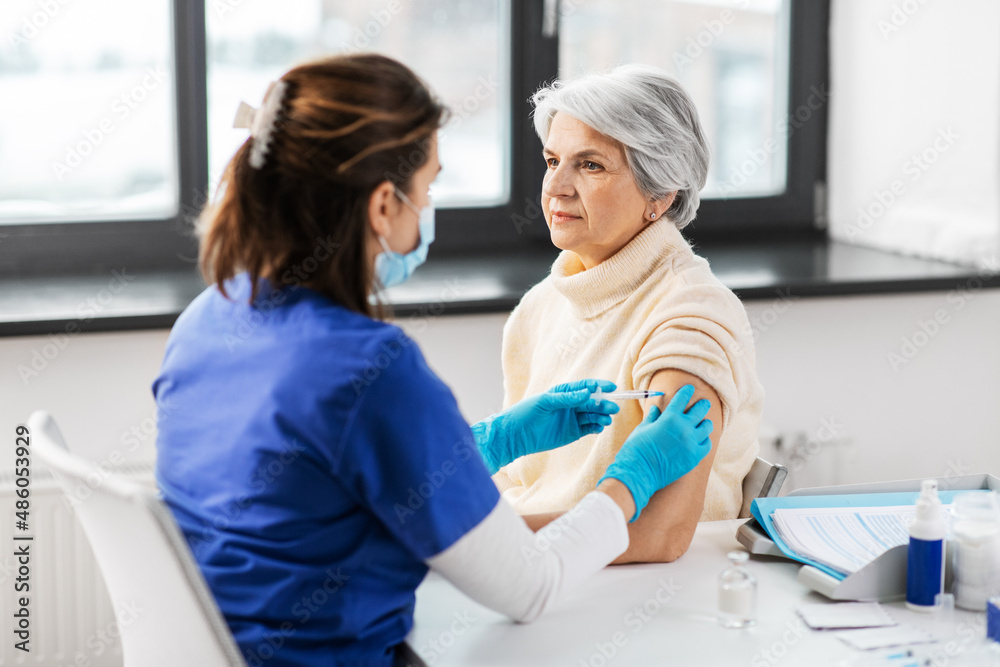 medicine, health and vaccination concept - doctor or nurse with syringe making vaccine or drug injection to senior woman at hospital medicine, health and vaccination concept - doctor or nurse with syringe making vaccine or drug injection to senior woman at hospital