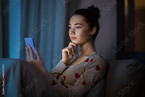 technology, bedtime and rest concept - pensive teenage girl in pajamas with smartphone sitting in bed at night photo