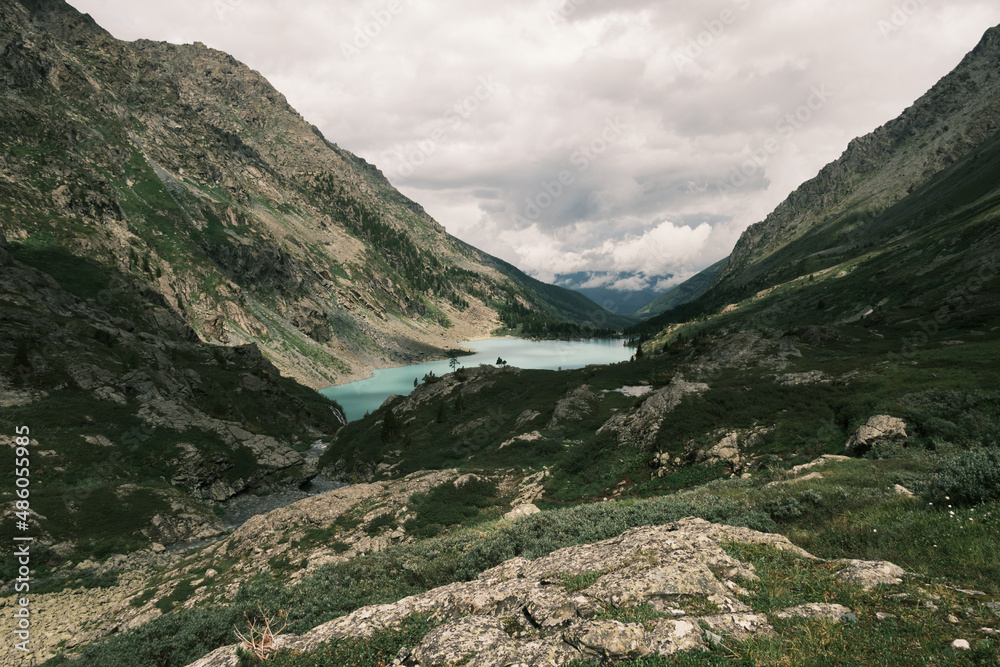 Fototapeta premium Landscape photography of the lake in the Altai mountains. Turquoise milk water, rocks, stones, junipers and clouds. Wallpaper, poster, postcard. Calm and peaceful concept.