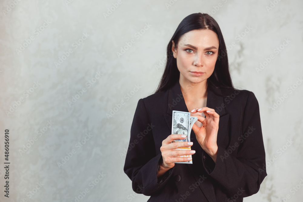 Young beautiful brunette woman in formal black suit holding dollar money wad. Passion and temptation concept Young beautiful brunette woman in formal black suit holding dollar money wad. Passion and temptation concept