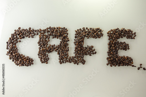 Das Wort Cafe geschrieben mit gold braunen gerösteten Kaffee Bohnen auf einer hellen Oberfläche