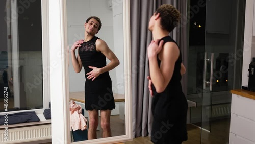 A man in little black dress in front the mirror sensually moves