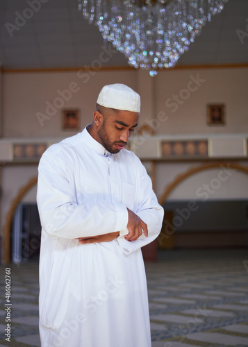 A portrait of young Muslim man standing with his arms crossed during prayers at a mosque with a beautiful chandelier in the background photo