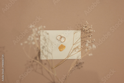 Wedding rings and invitations and craft envelopes on beigen background. Top view on paper cards, rings and dried flowers bouquet, copy space. Memmorable date organization concept photo