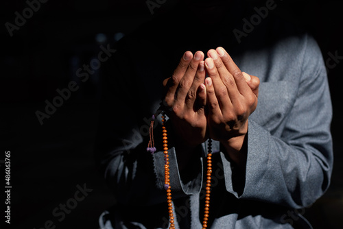 Close up of a Muslim man's hands in the sunlight praying and holding prayer beads