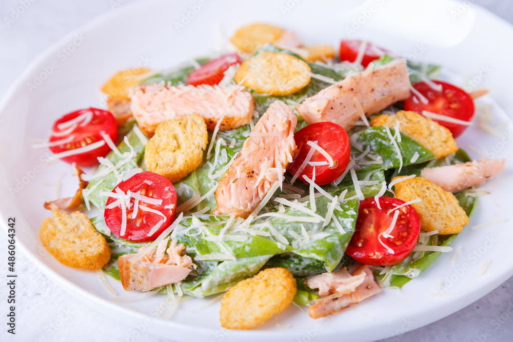 Caesar salad with red fish (salmon, trout), cherry tomatoes, croutons, parmesan cheese and romaine. Traditional American dish. Close-up, selective focus. Caesar salad with red fish (salmon, trout), cherry tomatoes, croutons, parmesan cheese and romaine. Traditional American dish. Close-up, selective focus.