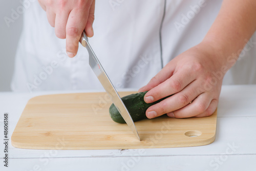 the hands of the cook cut the cucumber on a wooden board, on a white background