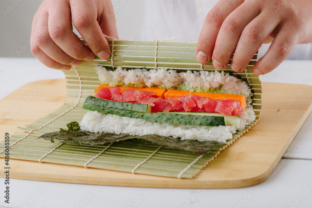 the chef cook prepares sushi and wraps a letter to the nori in the roll, on white background the chef cook prepares sushi and wraps a letter to the nori in the roll, on white background