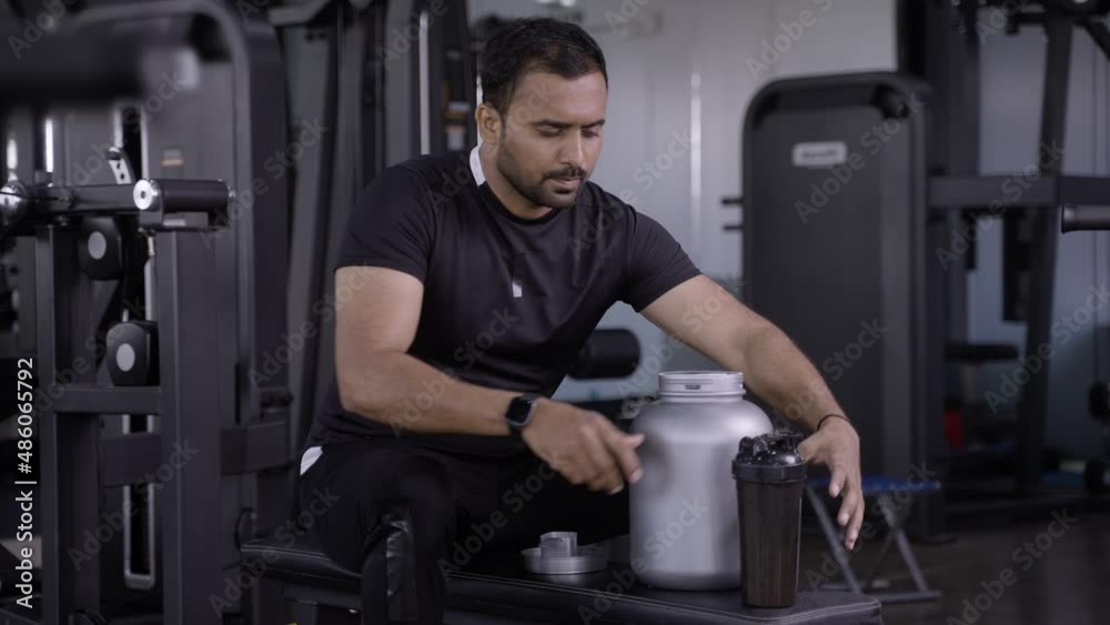 bodybuilder drinking or taking protein powder and mixing with water on bottle by shaking at gym - concpet of muscular gain, fitness training and workout