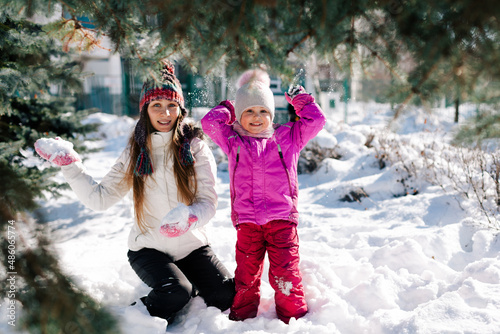 Caucasian woman and her little daughter looking at camera smiling having fun in sunny winter day. Horizontal headshot, side view. Soft focus on kid. Happy parenting and winter activities concept.