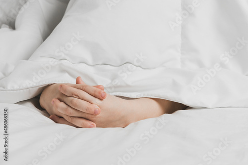 The childs hands are covered with white bed linen. The warmth of home comfort. © Evgenii