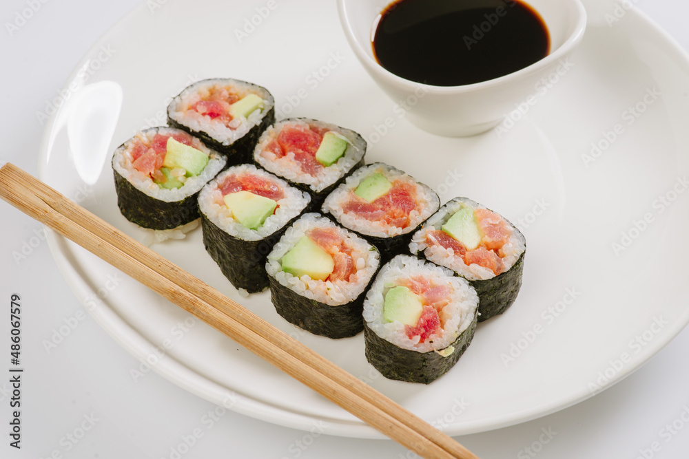 Sushi with chopsticks on a white plate. Sushi roll japanese food in restaurant isolated on white background. Fresh hosomaki pieces with rice and nori. Sushi with chopsticks on a white plate. Sushi roll japanese food in restaurant isolated on white background. Fresh hosomaki pieces with rice and nori.