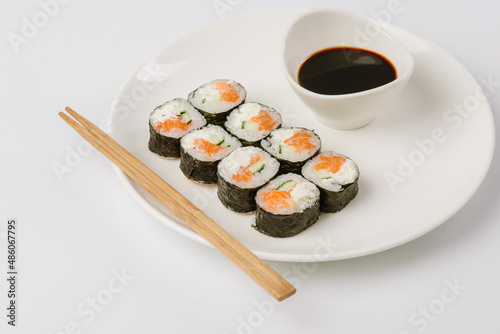 Sushi with chopsticks on a white plate. Sushi roll japanese food in restaurant isolated on white background. Fresh hosomaki pieces with rice and nori.