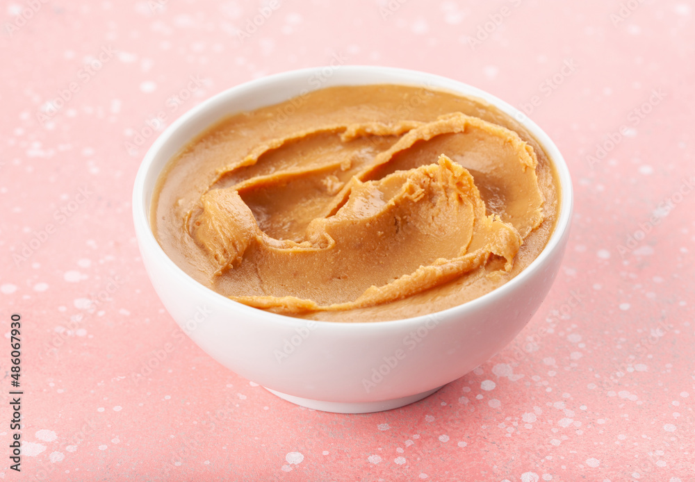smooth peanut butter in bowl on pink background smooth peanut butter in bowl on pink background