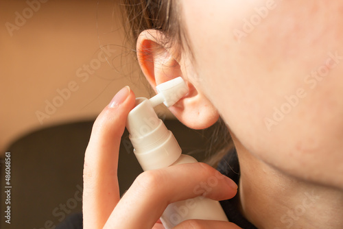 Woman uses an ear spray. Nozzle is installed in the ear hole. Daily hygiene and care of the ear canal. Horizontal photo.