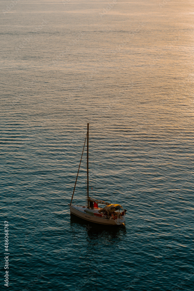 Fototapeta premium Boat docked by the sea in Ibiza. Overlooking rocky island, houses, sunrise, calm sea
