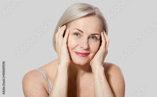Fifty year old woman is very pleased with her well-groomed face relaxed looking at the camera. Macro face. Realistic images with their own imperfections. Isolated on grey.