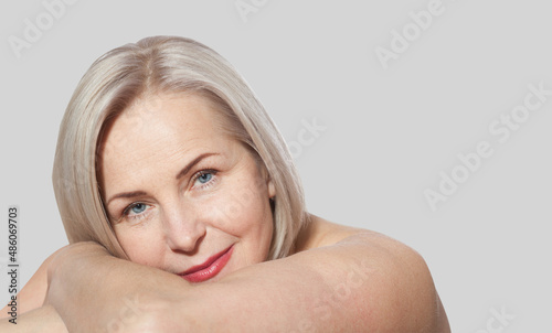 Fifty year old woman is very pleased with her well-groomed face relaxed looking at the camera. Macro face. Realistic images with their own imperfections. Isolated on grey.
