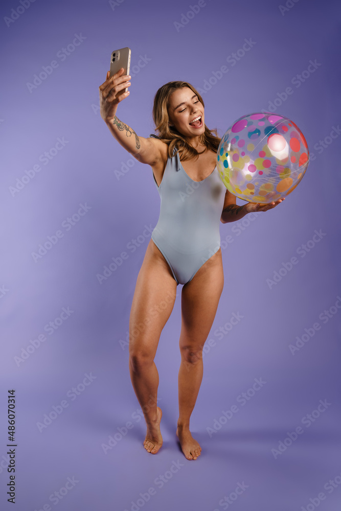 Young white woman in swimsuit taking selfie while holding beach ball Young white woman in swimsuit taking selfie while holding beach ball