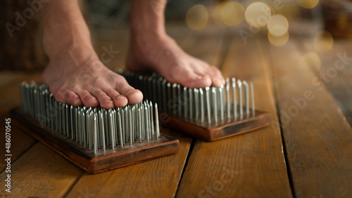 Male bare feet stand on a Sadhu boards with sharp nails on wooden floor indoor, close up, selected focus.