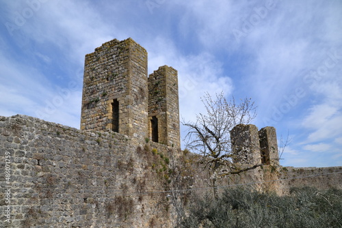 castle wall in Siena, Italy, with tall towers and with brown bricks and trees and blue sky in the background, in beautiful day