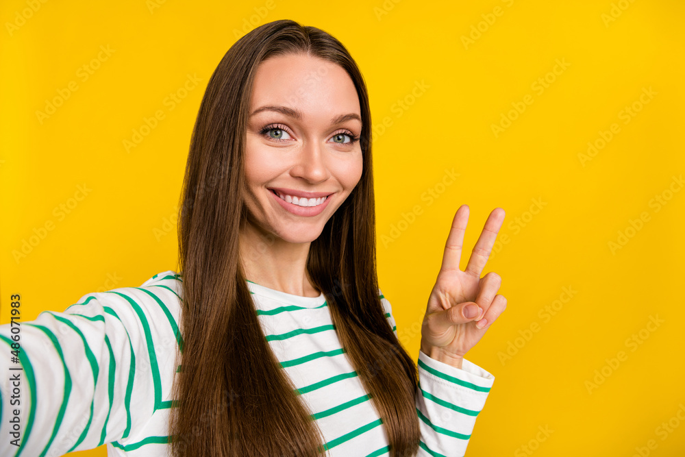 Photo of pretty adorable young woman wear striped showing v-sign tacking selfie isolated yellow color background Photo of pretty adorable young woman wear striped showing v-sign tacking selfie isolated yellow color background