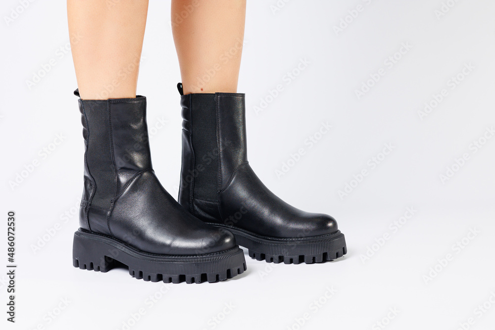 Legs of a woman in black leather boots from a new collection on a white background, legs of a girl in fashionable leather boots spring 2022.