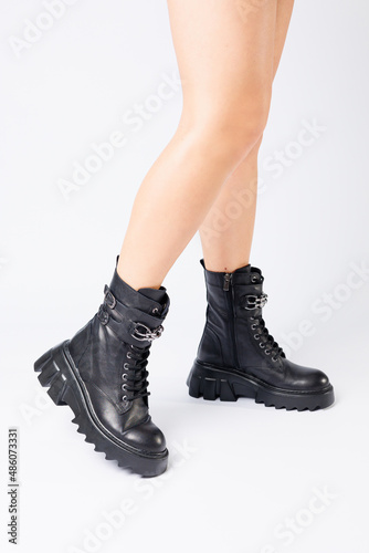 Legs of a woman in black leather boots from a new collection on a white background, legs of a girl in fashionable leather boots spring 2022.
