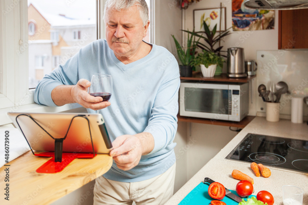 apartments. An elderly man with a glass of wine prepares food in the kitchen apartments. An elderly man with a glass of wine prepares food in the kitchen