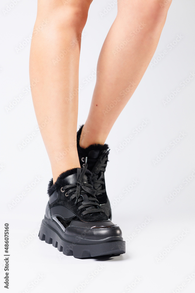 Fashionable black sneakers on the legs of a woman in the studio on a white background. Legs of a young girl with beautiful trendy shoes