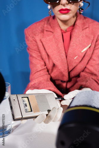 cropped view of blurred woman holding retro dictaphones near blurred microphones on blue background photo