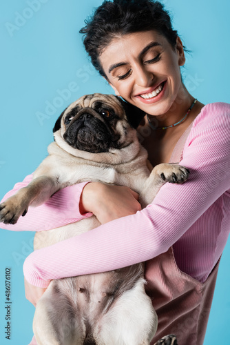 joyful woman with closed eyes cuddling funny pug isolated on blue © LIGHTFIELD STUDIOS