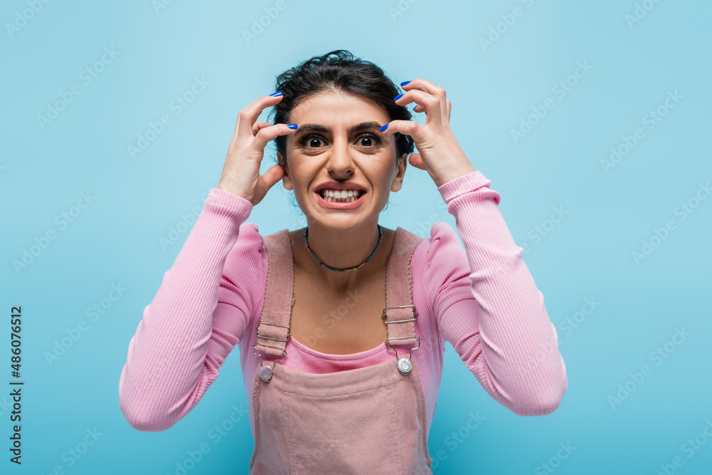 angry woman grimacing and gesturing while looking at camera isolated on blue angry woman grimacing and gesturing while looking at camera isolated on blue