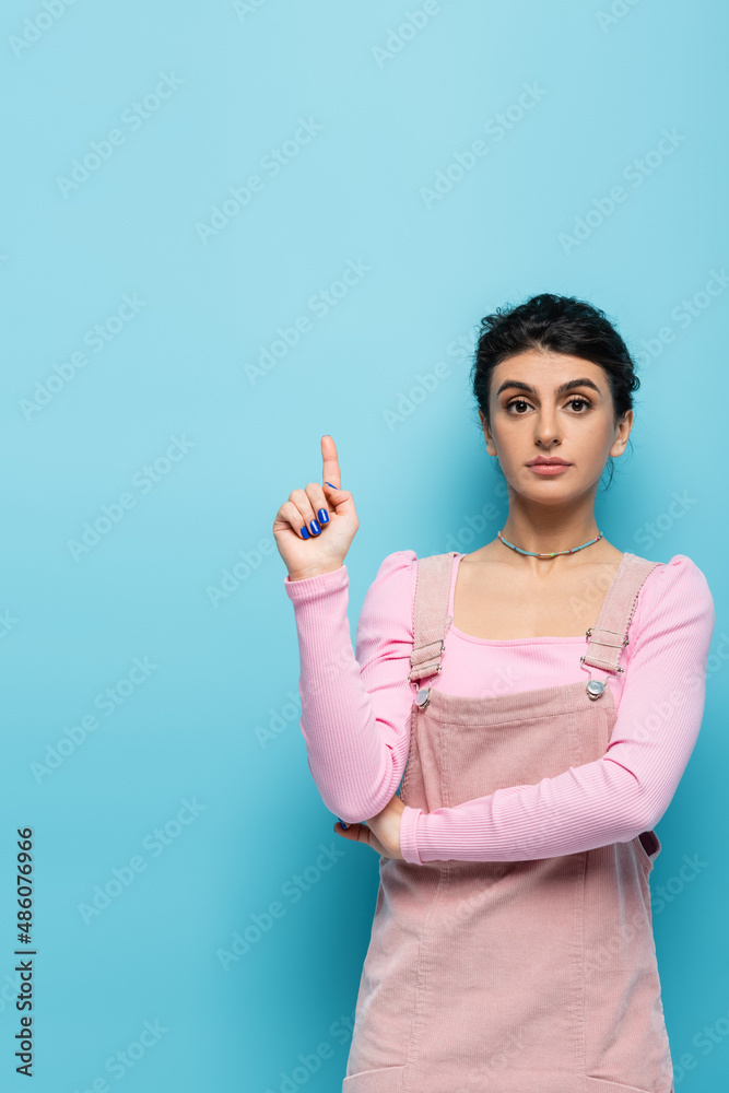 young and stylish woman pointing up with finger on blue background young and stylish woman pointing up with finger on blue background