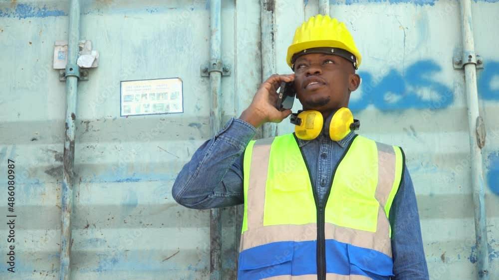 african american Foreman take a break talking on smartphone control loading Containers box at warehouse logistic in Cargo freight ship for import export. engineer at construction site african american Foreman take a break talking on smartphone control loading Containers box at warehouse logistic in Cargo freight ship for import export. engineer at construction site