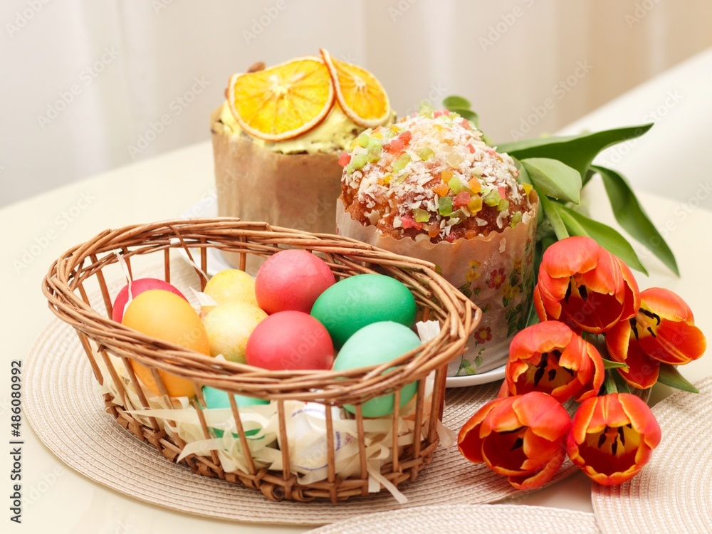 Easter cakes and colored eggs in a wicker basket on the festive table.