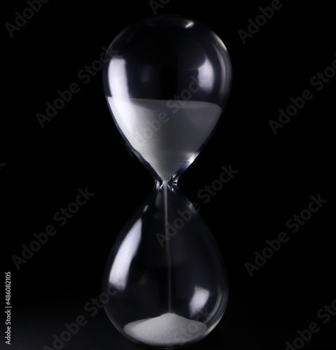 Hourglass with white sand showing time from low light. dark on a black background
