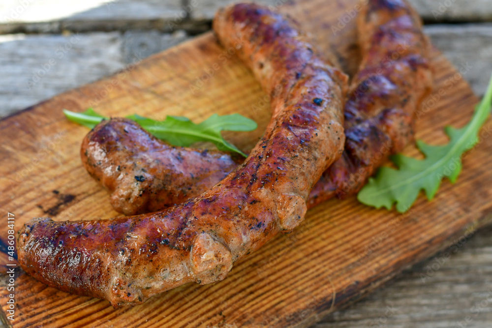 Fototapeta premium Grilled pork juicy sausages on wooden board outdoors. Grilling food, bbq, barbecue, picnic
