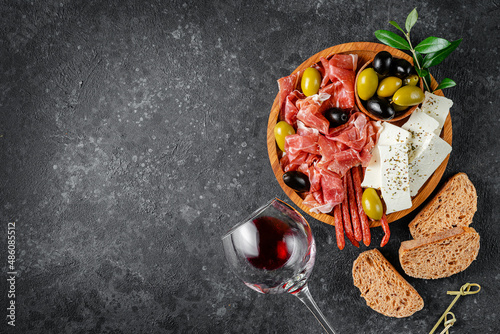 Tableau sur toile Appetizer wooden plate with meat, cheese and olives on dark concrete background