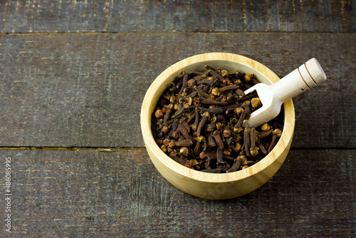 Cloves in wooden bowl with scoop on rustic wooden background. Herbal cloves have a fragrant and spicy flavor.