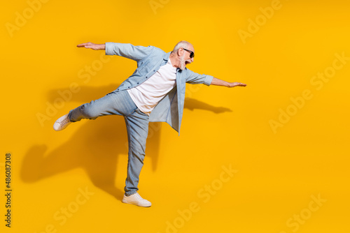 Full length body size view of attractive cheerful motivated grey-haired man having fun flying isolated on bright yellow color background