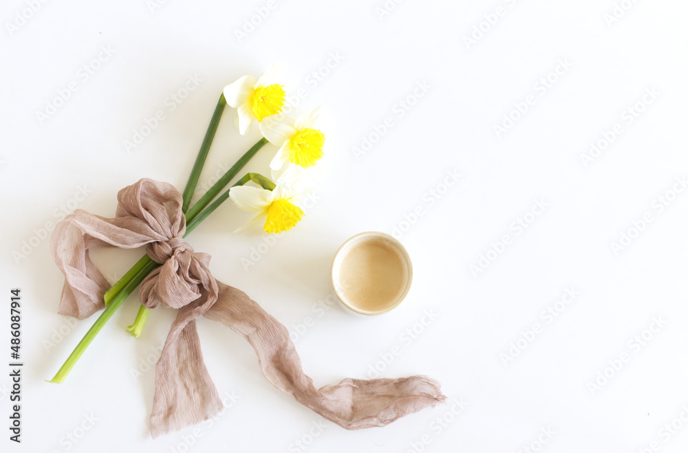 Spring wedding still life. Silk ribbon, narcissus daffodil flowers on a white. Cup of coffee with milk. Breakfast composition, Easter. Spring wedding still life. Silk ribbon, narcissus daffodil flowers on a white. Cup of coffee with milk. Breakfast composition, Easter.