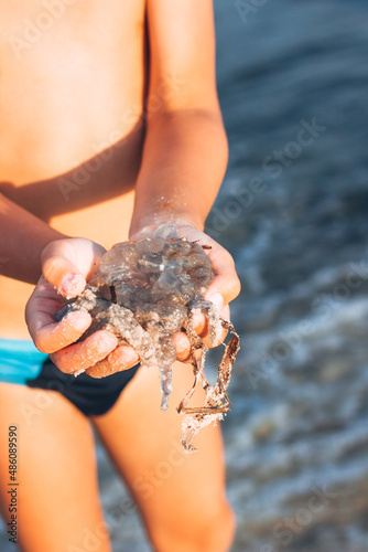 A small child stands on the beach with a jellyfish, the concept of a jellyfish invasion